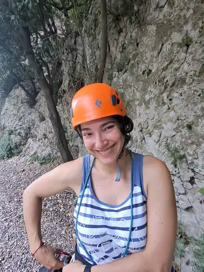 A climber in an orange helmet smiling at the foot of a rock face