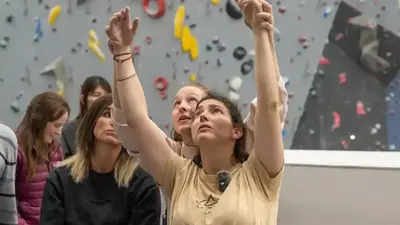 A group of people with their arms raised in front of a climbing wall